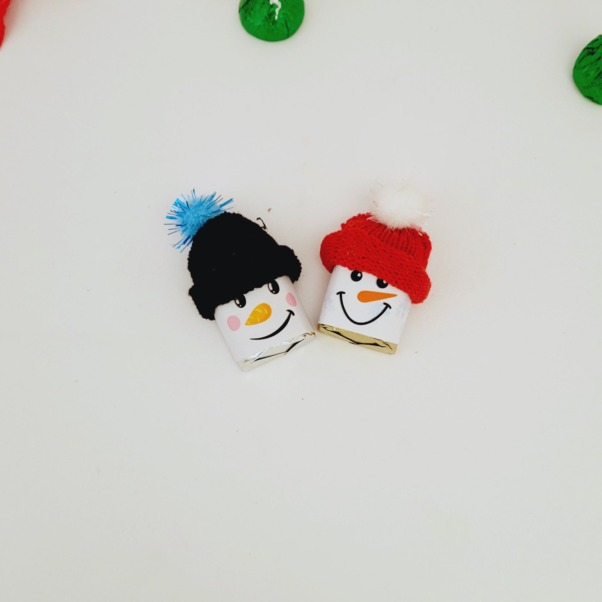 Two snowman-wrapped Hershey Nuggets with colorful hats on a white background
